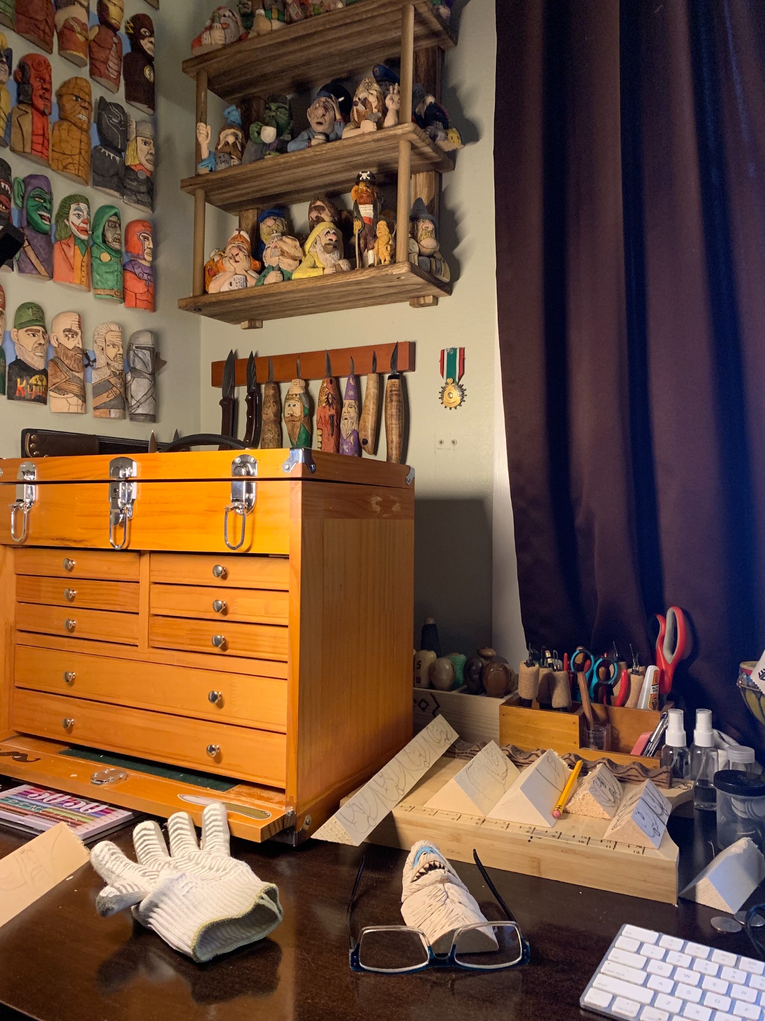 Marc's woodcarving workspace with carving knives, unfinished basswood figures, and shelves of completed carvings